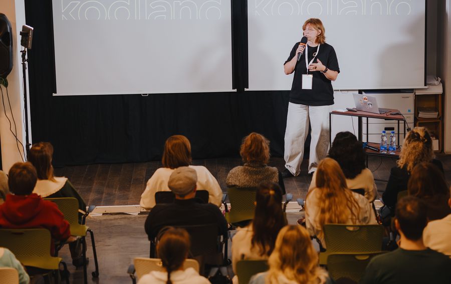 Viktoriia on stage with a microphone, facing a full room.