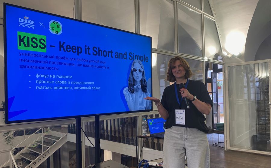 Viktoriia next to a screen with a training slide “KISS — Keep it Short and Simple”.